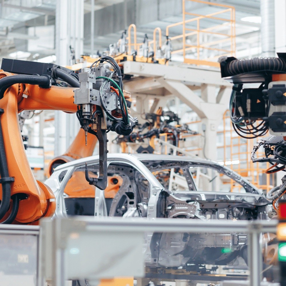 Orangefarbene Industrieroboter schweißen eine Karosserie in einer Automobilfabrik – Wärmedämmungen für die Automobilindustrie