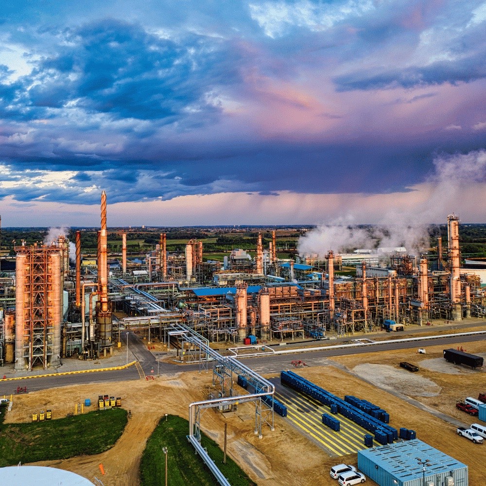 Petrochemische Anlage mit Kolonnen und Rohrbrücken unter dramatischem Abendhimmel – chemikalienbeständige Isolierungen