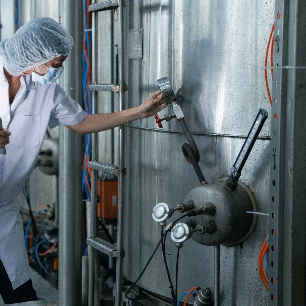 Mitarbeiterin mit Haube und Maske bedient Edelstahlarmaturen in einem Lebensmittelbetrieb – lebensmittelkonforme Isolierungen